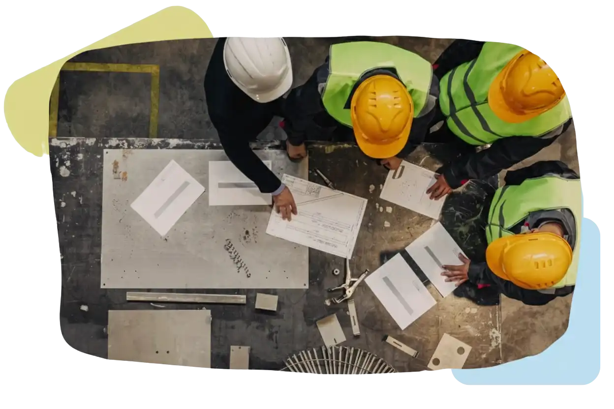 Overhead view of three construction workers in yellow safety vests and a supervisor in a suit examining architectural plans, representing Contractor Management by Remire.