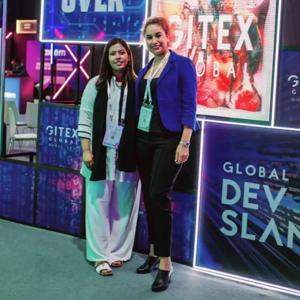 Two professional women standing in front of a digital GITEX Global display, illustrating the transition as Remire went fully remote.